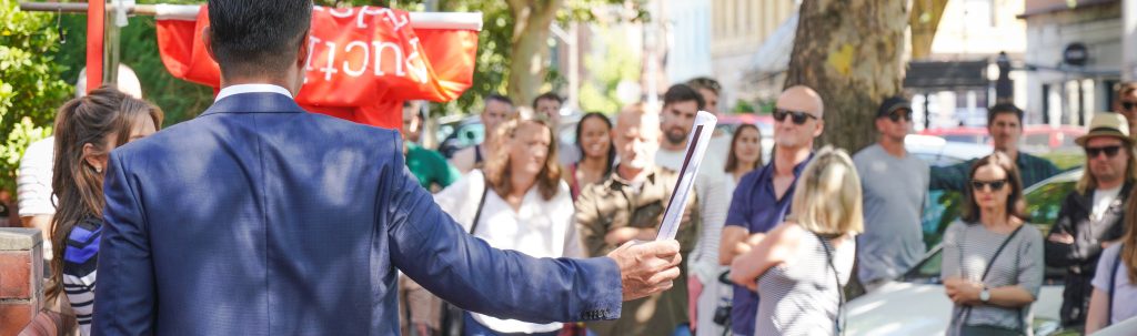 Auctioneer conducting property auction in front of large crowd